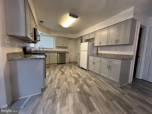 kitchen featuring gray cabinetry, dark stone countertops, appliances with stainless steel finishes, and light hardwood / wood-style flooring