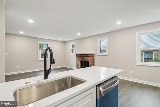 kitchen featuring white cabinets, a fireplace, stainless steel dishwasher, dark hardwood / wood-style floors, and sink