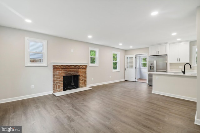 unfurnished living room with a brick fireplace, dark hardwood / wood-style floors, and sink