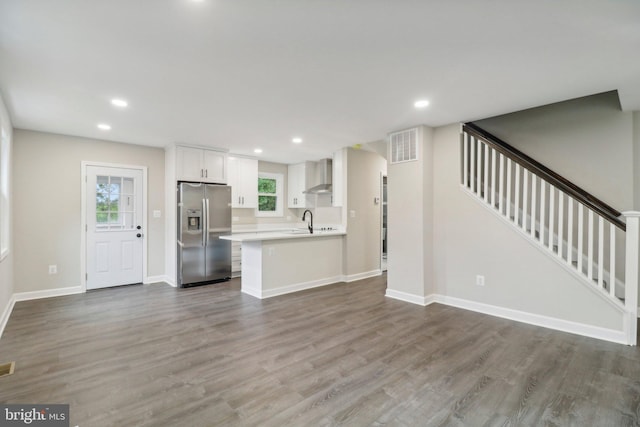 kitchen with stainless steel fridge with ice dispenser, sink, white cabinetry, wall chimney range hood, and hardwood / wood-style floors