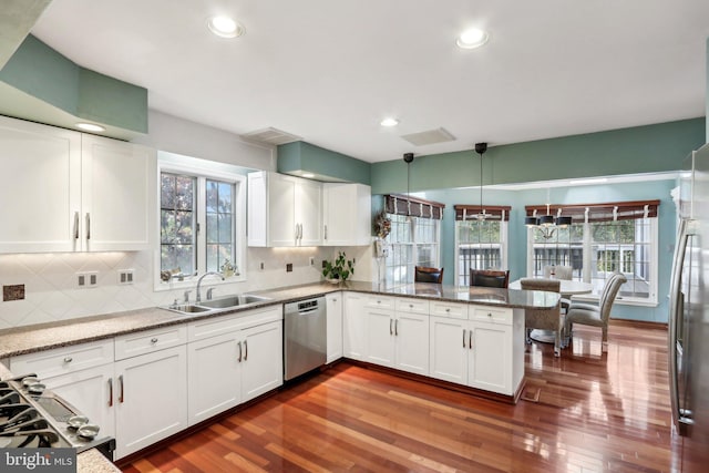 kitchen featuring dark wood-type flooring, sink, kitchen peninsula, hanging light fixtures, and appliances with stainless steel finishes