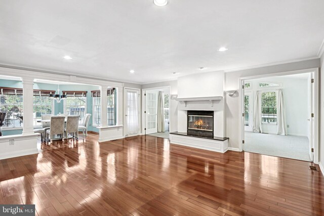 unfurnished living room featuring ornamental molding, decorative columns, and hardwood / wood-style floors