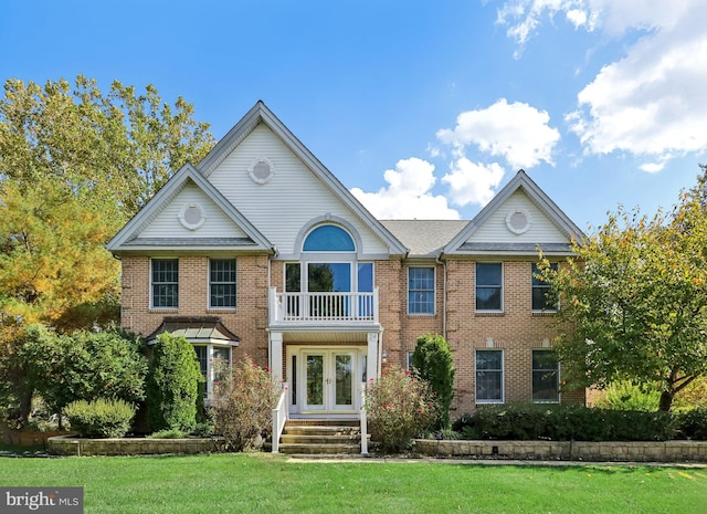 view of front facade with a front yard, a balcony, and french doors