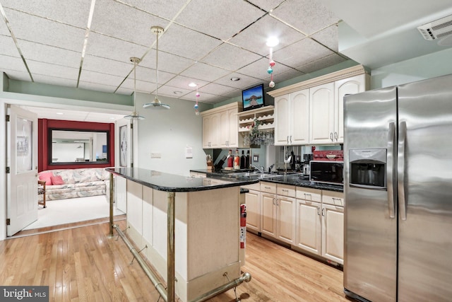 kitchen featuring stainless steel fridge, light wood-type flooring, pendant lighting, a breakfast bar, and a center island