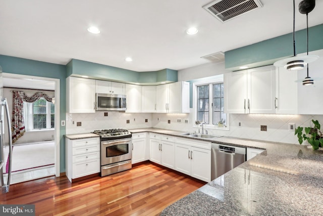 kitchen with pendant lighting, white cabinets, sink, stainless steel appliances, and light wood-type flooring