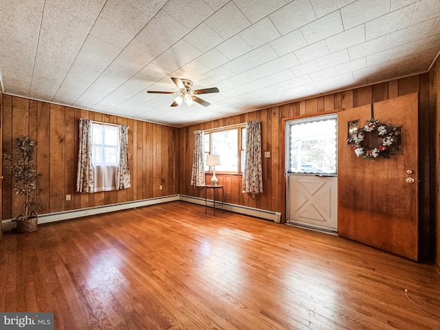 unfurnished room featuring wood walls, hardwood / wood-style floors, baseboard heating, and ceiling fan