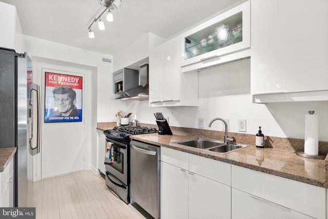 kitchen featuring sink, wall chimney range hood, appliances with stainless steel finishes, light stone counters, and white cabinets