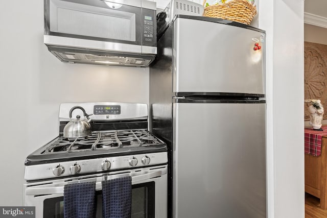 kitchen with appliances with stainless steel finishes, crown molding, and hardwood / wood-style floors