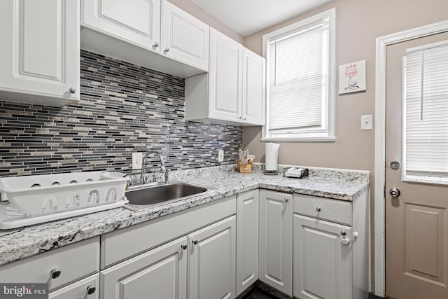 kitchen featuring white cabinets, backsplash, light stone countertops, and sink