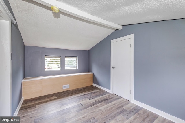 unfurnished room with a textured ceiling, lofted ceiling with beams, and hardwood / wood-style floors