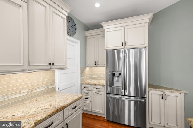 kitchen with light stone countertops, dark hardwood / wood-style flooring, stainless steel refrigerator with ice dispenser, backsplash, and white cabinets