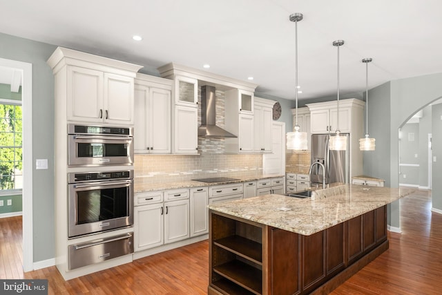 kitchen with pendant lighting, a center island with sink, sink, wall chimney exhaust hood, and stainless steel appliances