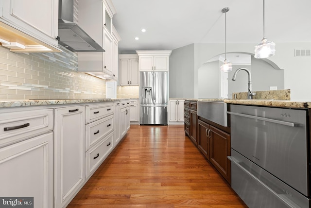 kitchen with wall chimney exhaust hood, decorative backsplash, white cabinetry, and appliances with stainless steel finishes