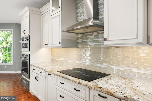 kitchen with white cabinets, wall chimney range hood, black electric cooktop, light stone counters, and dark hardwood / wood-style flooring