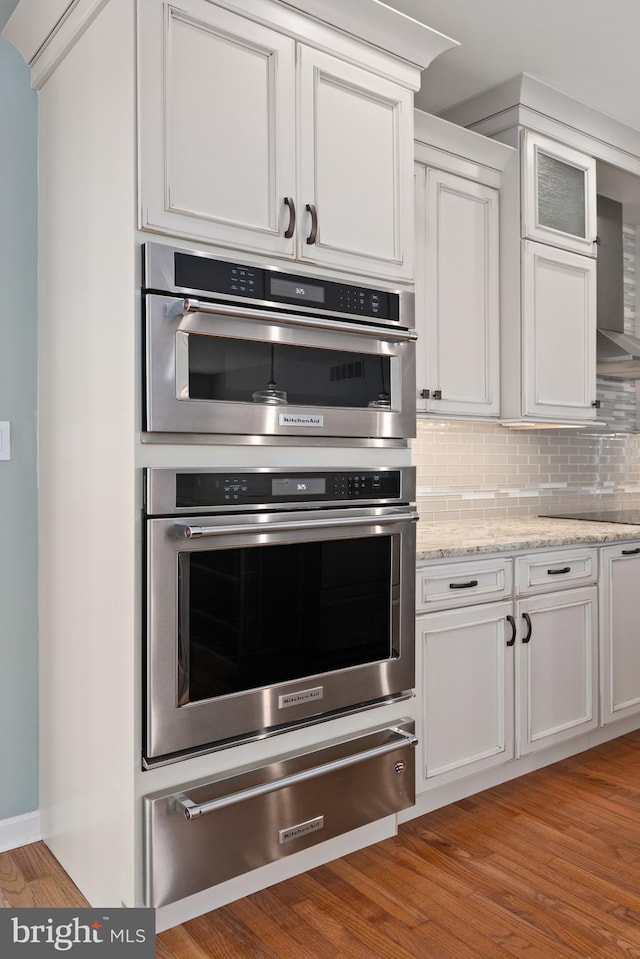 kitchen featuring backsplash, white cabinets, light hardwood / wood-style floors, light stone counters, and stainless steel double oven