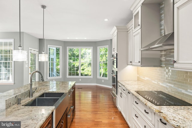 kitchen featuring light stone countertops, wall chimney range hood, decorative light fixtures, black electric stovetop, and white cabinets