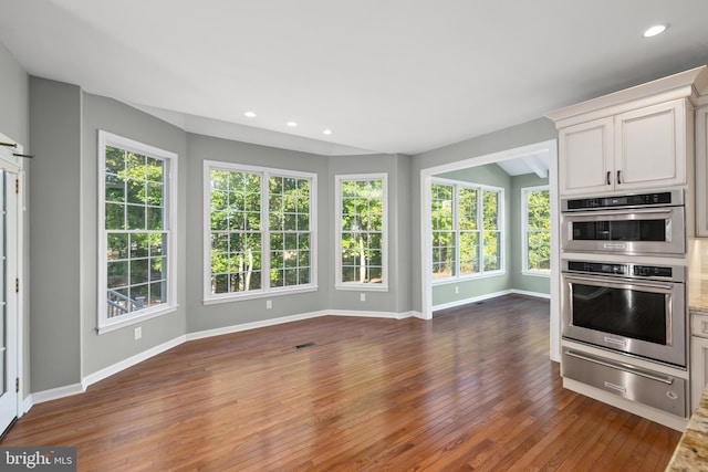 kitchen featuring light stone countertops, stainless steel double oven, vaulted ceiling, dark wood-type flooring, and white cabinets