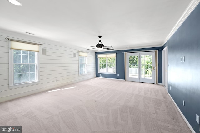 carpeted empty room with ceiling fan, wood walls, and crown molding