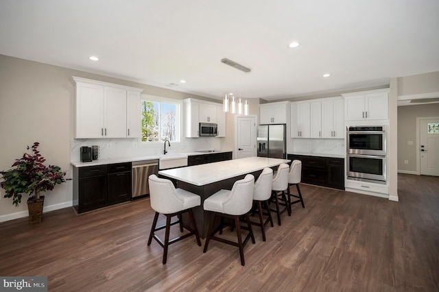 kitchen featuring a center island, hanging light fixtures, stainless steel appliances, dark hardwood / wood-style floors, and a kitchen bar