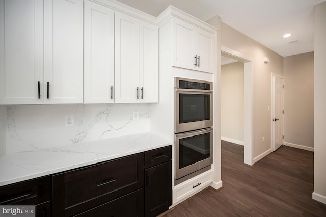 kitchen with light stone countertops, dark hardwood / wood-style flooring, double oven, backsplash, and white cabinets