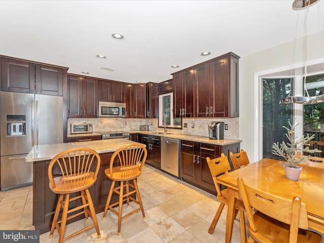 kitchen featuring appliances with stainless steel finishes, backsplash, a kitchen island, a breakfast bar area, and dark brown cabinets