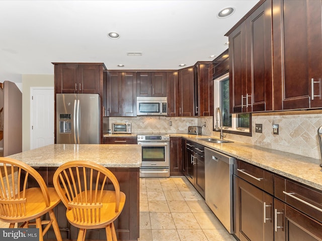 kitchen featuring light stone counters, sink, tasteful backsplash, stainless steel appliances, and a breakfast bar