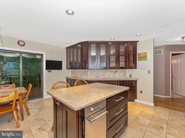 kitchen with decorative backsplash, light stone counters, a center island, and dark brown cabinetry