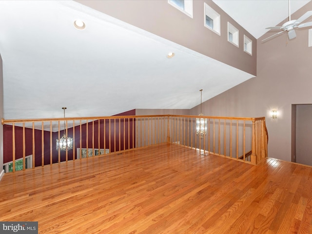 spare room featuring ceiling fan with notable chandelier, wood-type flooring, and high vaulted ceiling