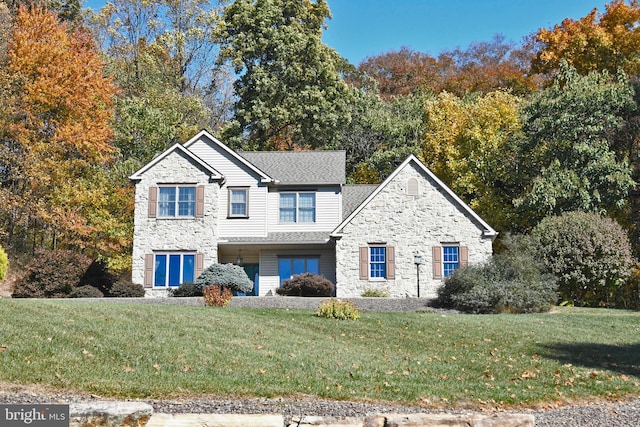 view of front of house featuring a shingled roof, a front lawn, and stone siding