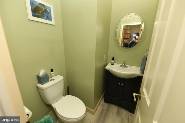 half bathroom with wood finished floors, toilet, and vanity