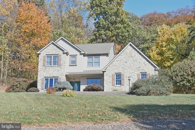 traditional-style house with roof with shingles, a front yard, and stone siding