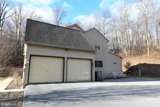 view of side of property with a garage, a shingled roof, and driveway