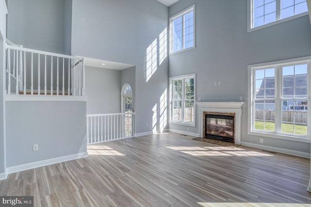 unfurnished living room with a towering ceiling, light hardwood / wood-style floors, and plenty of natural light