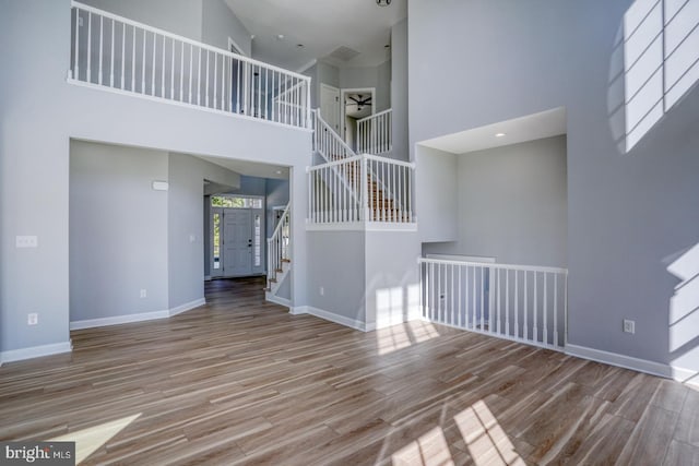 unfurnished living room with a high ceiling, light hardwood / wood-style floors, and ceiling fan