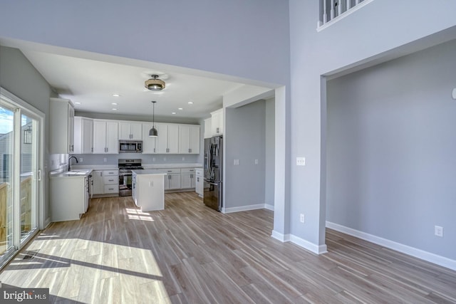 kitchen with white cabinets, appliances with stainless steel finishes, sink, light hardwood / wood-style floors, and a center island