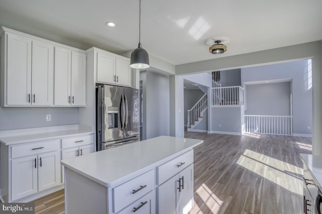 kitchen with stainless steel refrigerator with ice dispenser, white cabinets, hardwood / wood-style flooring, and pendant lighting