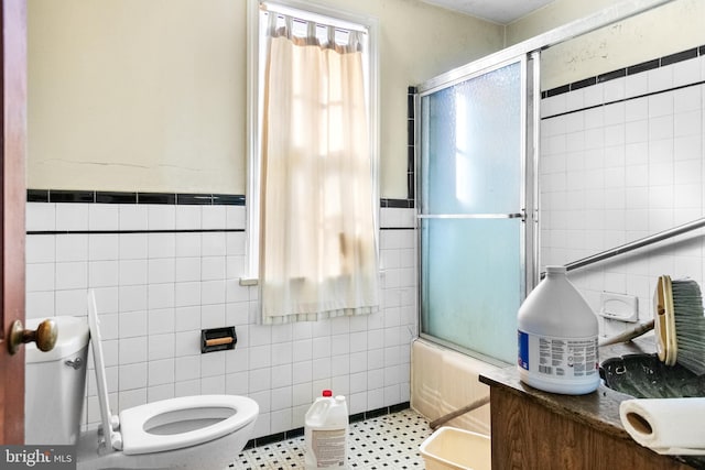 bathroom with tile patterned floors, toilet, combined bath / shower with glass door, and tile walls