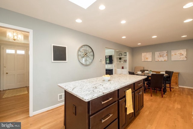 kitchen featuring a kitchen island, light stone countertops, dark brown cabinetry, and light hardwood / wood-style floors