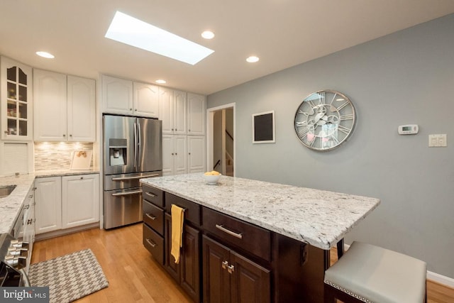 kitchen featuring a skylight, a kitchen island, dark brown cabinets, light hardwood / wood-style floors, and stainless steel fridge with ice dispenser