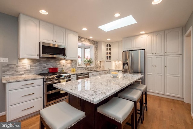 kitchen with light stone countertops, white cabinetry, stainless steel appliances, and light hardwood / wood-style floors