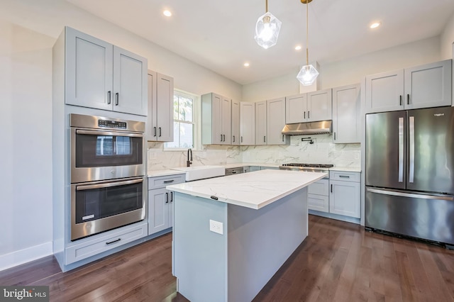 kitchen featuring light stone counters, a center island, stainless steel appliances, dark wood-type flooring, and sink