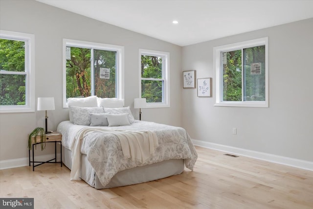 bedroom featuring lofted ceiling, light hardwood / wood-style floors, and multiple windows