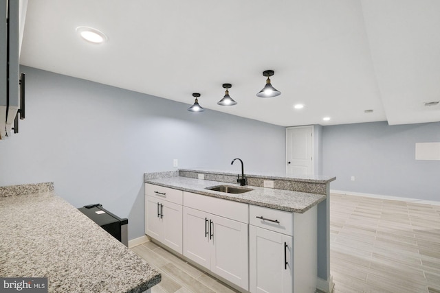 kitchen featuring a center island with sink, light stone countertops, white cabinetry, and sink