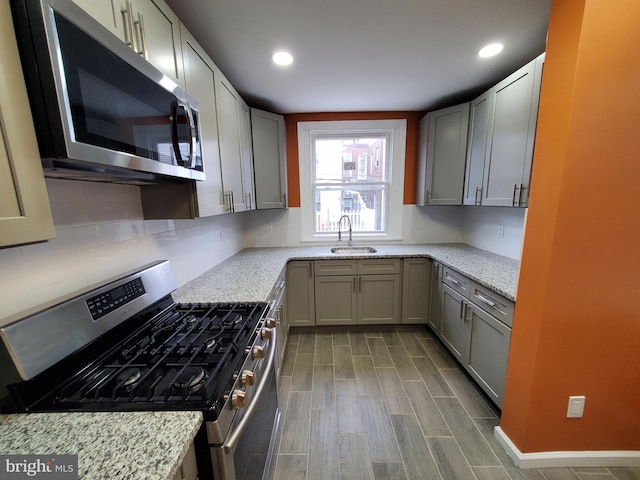 kitchen with light stone counters, sink, gray cabinetry, appliances with stainless steel finishes, and dark hardwood / wood-style flooring