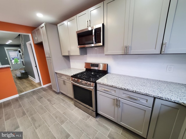 kitchen featuring light stone countertops, gray cabinetry, light hardwood / wood-style floors, and appliances with stainless steel finishes