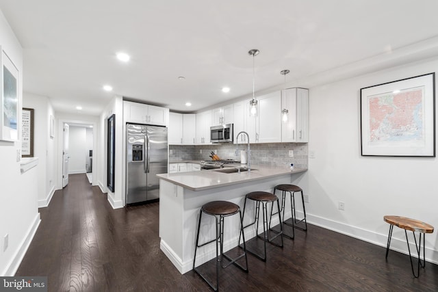 kitchen featuring stainless steel appliances, white cabinets, dark hardwood / wood-style flooring, kitchen peninsula, and decorative light fixtures