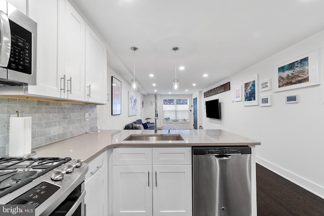 kitchen featuring kitchen peninsula, decorative light fixtures, white cabinetry, appliances with stainless steel finishes, and dark hardwood / wood-style flooring