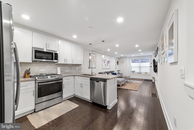 kitchen featuring dark hardwood / wood-style floors, stainless steel appliances, kitchen peninsula, pendant lighting, and white cabinetry