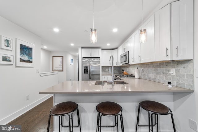 kitchen featuring white cabinets, hanging light fixtures, kitchen peninsula, dark wood-type flooring, and appliances with stainless steel finishes