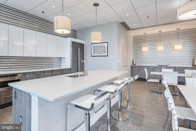 kitchen with appliances with stainless steel finishes, decorative backsplash, white cabinets, pendant lighting, and a center island with sink